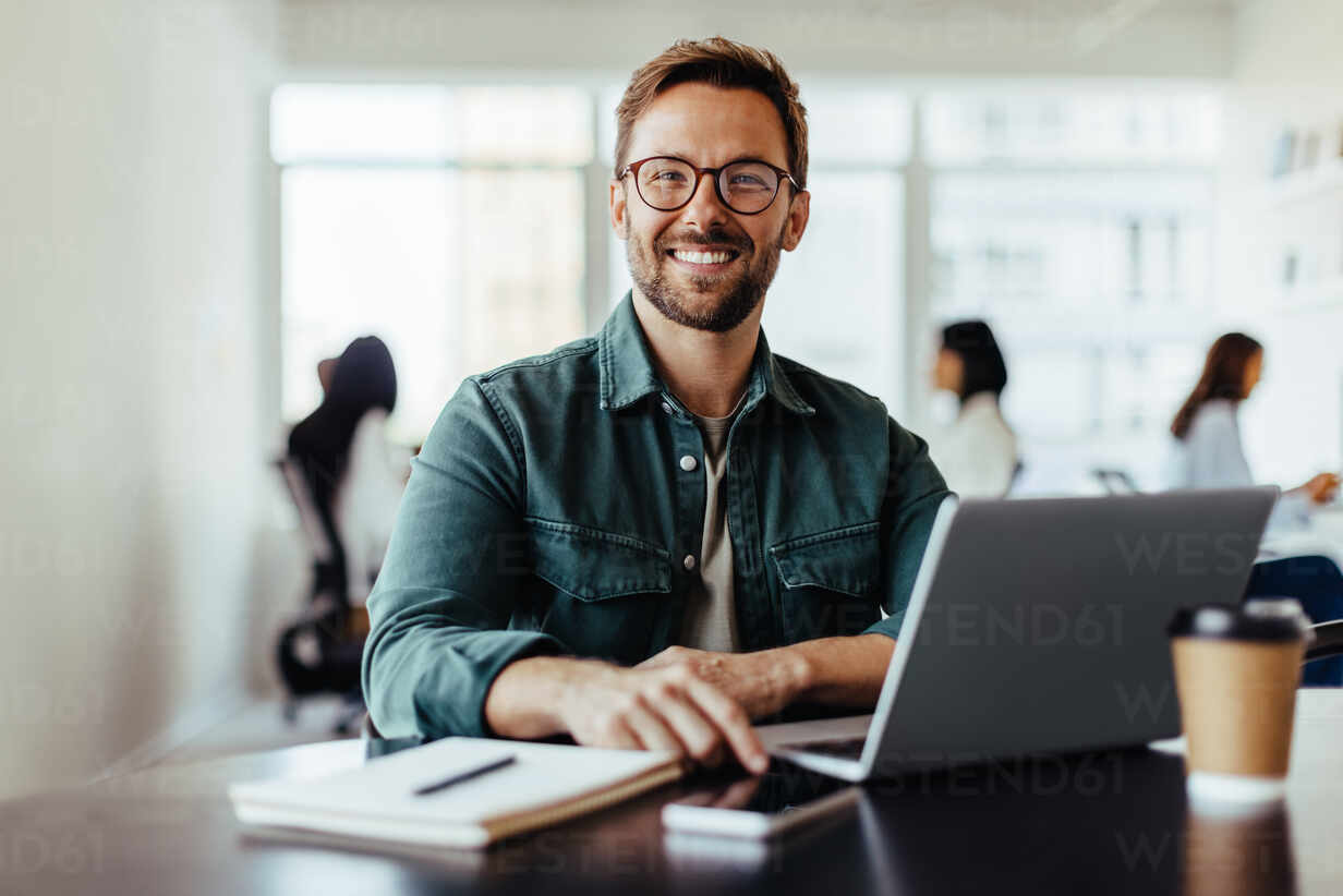 portrait-of-a-business-man-sitting-in-an-office-with-his-colleagues-in-the-background-happy-business-man-working-in-a-co-working-office-jlpsf28798